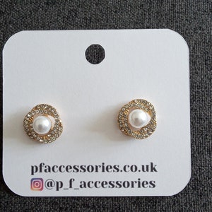 May include: A pair of gold-tone stud earrings with a white pearl center and a halo of clear rhinestones. The earrings are displayed on a white card with the text "pfaccessories.co.uk @p_f_accessories".
