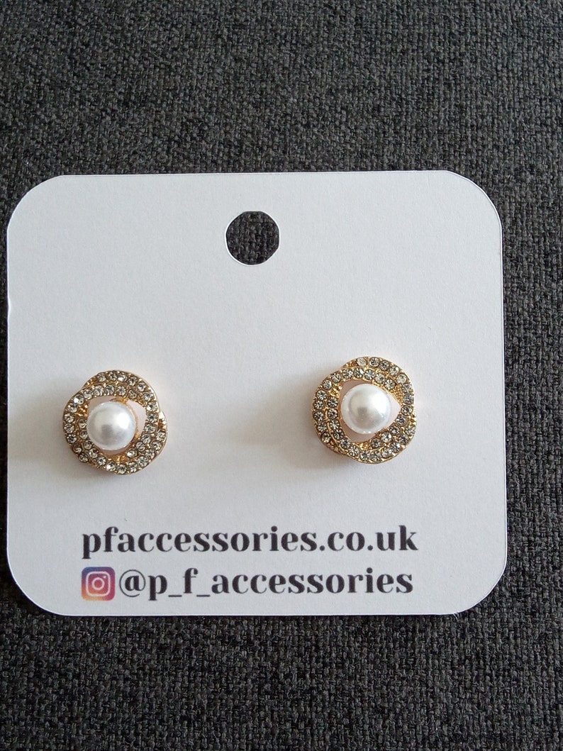May include: A pair of gold-tone stud earrings with a white pearl center and a halo of clear rhinestones. The earrings are displayed on a white card with the text "pfaccessories.co.uk @p_f_accessories".