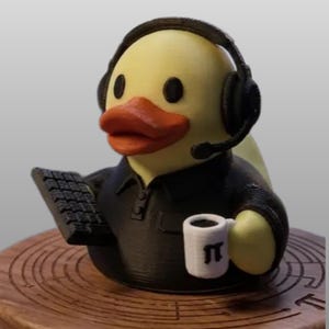 May include: A yellow rubber duck figurine wearing black headphones and a black collared shirt. The duck holds a small black keyboard in one wing and a white mug with a black pi symbol printed on the side in the other wing. The duck has an orange beak.