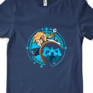 May include: A navy blue t-shirt featuring a graphic of a character from the Legend of Zelda video game series. The character is holding a sword and shield, and the graphic is surrounded by a blue circle with geometric designs.