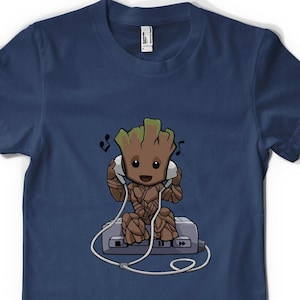 May include: A navy blue t-shirt featuring a cartoon image of a green character wearing headphones and sitting on a cassette player. The character is smiling and has musical notes around its head.