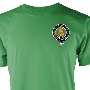 May include: A green t-shirt with a circular emblem depicting a cat and the words "TOUCH NOT THE CAT BUT A GLOVE". The emblem is in orange, blue, red, and white. The shirt is made of a soft material.
