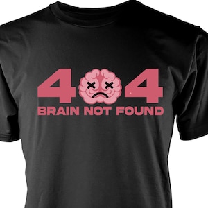 May include: Black t-shirt with a pink 404 graphic. The graphic features a pink brain with a sad face and two X's for eyes. The text "BRAIN NOT FOUND" is below the graphic.