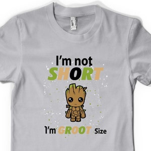 May include: A grey t-shirt with a green and orange graphic of a cartoon character. The text "I'm not SHORT I'm GROOT Size" is printed on the shirt.
