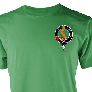 May include: Green t-shirt with a crest design. The crest features a brown animal, red and white details, and the words "SANS PEUR" in a circle. The shirt is made of a soft material.