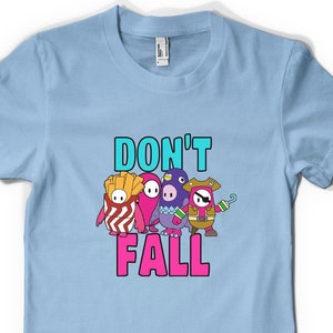 May include: Light blue t-shirt featuring a graphic of four Fall Guys characters and the text "Don't Fall".