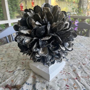 May include: A decorative sphere made of oyster shells, painted white, and mounted on a white pedestal. The sphere is on a white tablecloth with a colorful pattern.