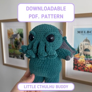 Op de afbeelding: Een groenblauw gehaakt knuffeltje met een Cthulhu-ontwerp, voorzien van grote zwarte ogen, meerdere tentakels rond de mond en kleine vleugels op de rug. De afbeelding bevat de tekst DOWNLOADABLE PDF. PATTERN en LITTLE CTHULHU BUDDY.