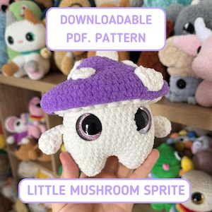May include: A crocheted mushroom sprite with a purple cap and white spots. The mushroom has large, black eyes with glitter accents. The image includes the text "DOWNLOADABLE PDF. PATTERN" and "LITTLE MUSHROOM SPRITE".