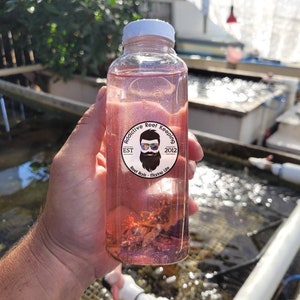 May include: A clear plastic bottle with a pink liquid and a white label that says "Proactive Reef Keeping Est. 2012 Reef Rock Marine Life".
