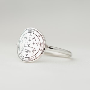 Könnte beinhalten: Ein silberner Ring mit einer kreisförmigen Oberfläche mit eingravierten Symbolen und dem Wort "URIEL". Der Ring hat einen dünnen Ring und ein detailliertes Design auf der Oberfläche, mit zusätzlichem Text am Rand.