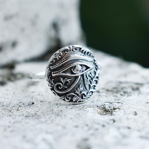 May include: Silver ring with an ornate design featuring the Eye of Horus, a symbol of protection and good luck in ancient Egyptian mythology.