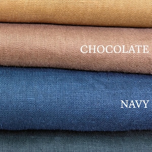 May include: Four stacked layers of woven fabric in distinct colors. The top layer is labeled HAZELNUT, followed by a layer labeled CHOCOLATE, a layer labeled NAVY, and a bottom layer labeled BLACK. Each fabric shows a visible, textured weave pattern.