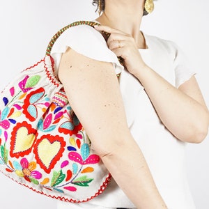 May include: A white fabric tote bag with a colourful embroidered design featuring hearts, flowers, and leaves. The embroidery is done in shades of red, pink, yellow, blue, and green.