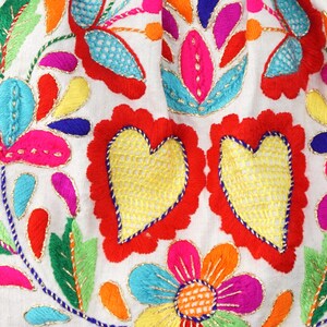May include: A piece of colourful embroidered fabric featuring a floral design and two red hearts. The fabric is white with gold thread accents.