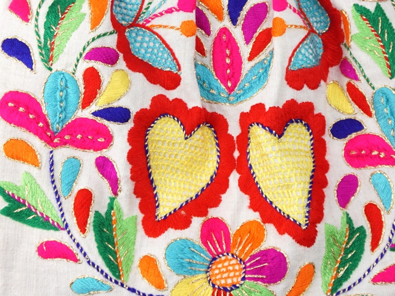 May include: A piece of colourful embroidered fabric featuring a floral design and two red hearts. The fabric is white with gold thread accents.