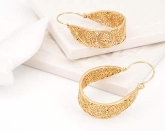 May include: A pair of gold hoop earrings featuring intricate filigree metalwork. The earrings have a curved, open-ended design with a delicate, lace-like pattern of swirling wire loops throughout the entire surface of the gold-toned metal hoops.