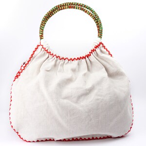 May include: A white canvas tote bag with a red stitched trim and a green and yellow woven handle.