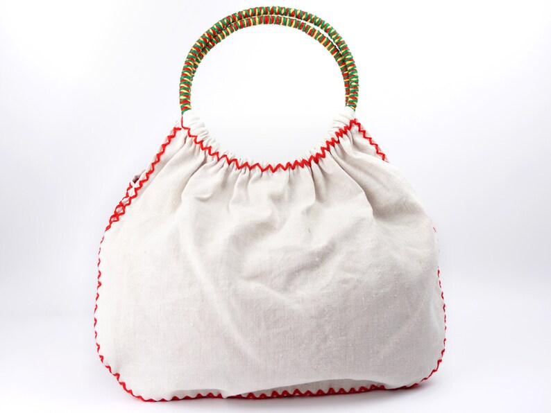 May include: A white canvas tote bag with a red stitched trim and a green and yellow woven handle.