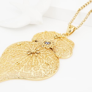 May include: A gold filigree pendant necklace with a heart-shaped design and a blue gemstone accent. The necklace features intricate details and a delicate chain.