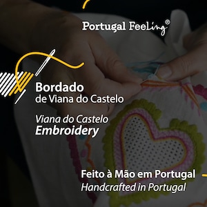 May include: A close-up of a hand embroidering a white fabric with colourful thread. The fabric has a heart design with a pink and green border. The text "Bordado de Viana do Castelo" and "Viana do Castelo Embroidery" is visible. The text "Feito &agrave; M&atilde;o em Portugal" and "Handcrafted in Portugal" is also visible.