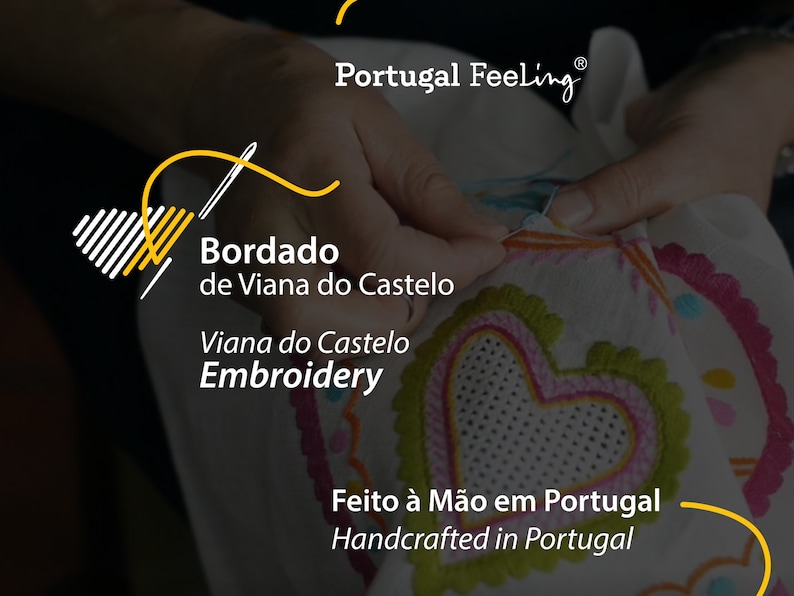 May include: A close-up of a hand embroidering a white fabric with colourful thread. The fabric has a heart design with a pink and green border. The text "Bordado de Viana do Castelo" and "Viana do Castelo Embroidery" is visible. The text "Feito &agrave; M&atilde;o em Portugal" and "Handcrafted in Portugal" is also visible.