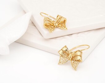 May include: A pair of gold-toned earrings featuring a bow-shaped design. Each earring is crafted with intricate filigree wirework, creating a delicate, open-patterned texture. The earrings are suspended from curved ear wires for secure placement.