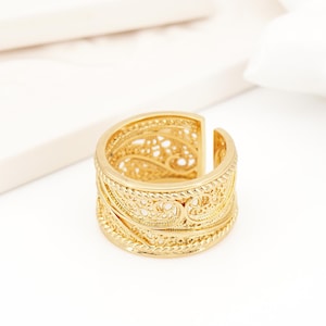 Pode incluir: Um anel de ouro com um design de filigrana intrincado. O anel é largo e tem uma forma arredondada.