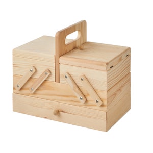 May include: A wooden storage box with a hinged lid, a pull-out drawer, and a carrying handle. The box is made of light-coloured wood and has a natural finish.