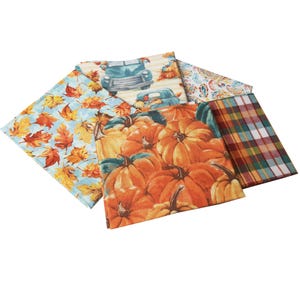 May include: Five fabric squares with different autumn-themed prints. One square features a blue truck with pumpkins, another has a plaid pattern, another has a paisley pattern, another has a blue background with orange and yellow leaves, and the last square has a close-up of orange pumpkins.