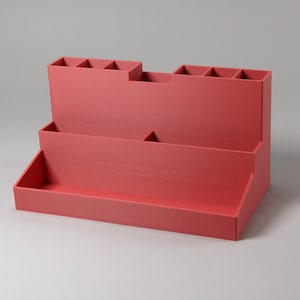 May include: A red plastic organiser with multiple compartments for storing small items. The organiser has two levels and a large open space on the bottom.