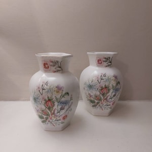 May include: Two white ceramic vases with a floral pattern. The vases are octagonal in shape and have a gold trim around the top.