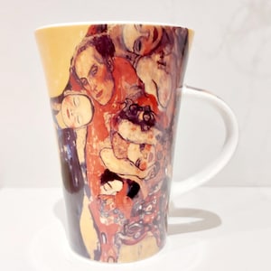 May include: A tall, tapered ceramic mug featuring a vibrant, multi-coloured artistic print of several human faces and figures in shades of yellow, orange, red, and dark brown. The mug has a smooth white interior and a curved white handle on the side.