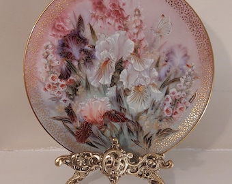 May include: A decorative porcelain plate with a floral design featuring a bouquet of white, pink, and purple irises with a butterfly. The plate is on a gold metal stand.