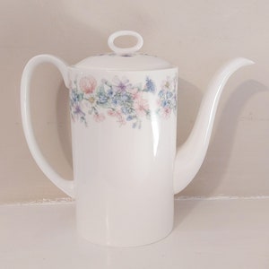 May include: White ceramic coffee pot with a floral design in shades of pink, blue, and green. The pot has a lid with a ring handle.