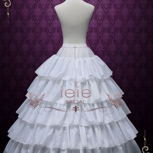 Puede incluir: Enaguas blancas de varias capas con una falda con volantes. La enagua est&aacute; en un maniqu&iacute; blanco sobre un fondo morado. El texto "ieie BRIDAL" est&aacute; impreso en la enagua.