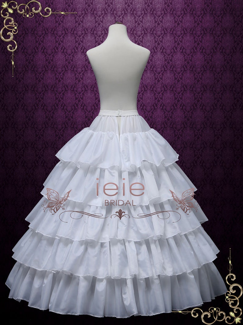 Puede incluir: Enaguas blancas de varias capas con una falda con volantes. La enagua est&aacute; en un maniqu&iacute; blanco sobre un fondo morado. El texto "ieie BRIDAL" est&aacute; impreso en la enagua.