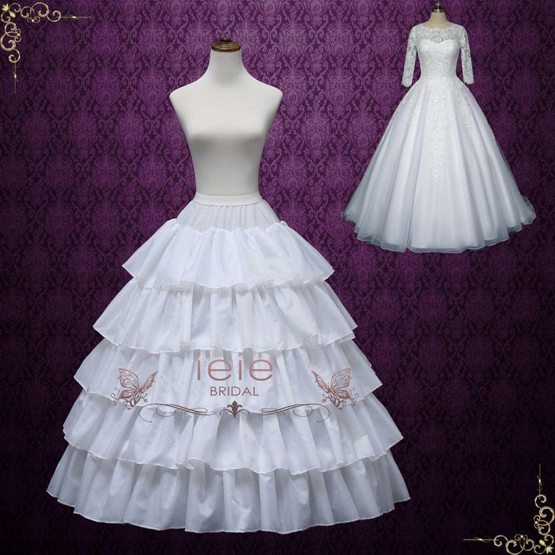 Puede incluir: Un enagua de tul blanco con m&uacute;ltiples capas, creando una silueta completa y voluminosa. La enagua est&aacute; dise&ntilde;ada para ser usada debajo de un vestido de novia u otra vestimenta formal. La enagua est&aacute; hecha de tul suave y c&oacute;modo y tiene un acabado liso. La enagua se muestra con un vestido de novia blanco con detalles de encaje. La enagua est&aacute; etiquetada "lele bridal".