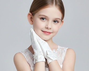 Puede incluir: Guantes de satén blanco con lazos y detalles de perlas. Los guantes están diseñados para un niño y probablemente para una ocasión especial. Los lazos están en la muñeca y los guantes son de color blanco liso.