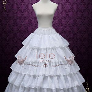 Puede incluir: Un enaguas blanco de varias capas con un borde con volantes. El enaguas est&aacute; en un maniqu&iacute; blanco sobre un fondo morado. El texto "ieie BRIDAL" es visible en el enaguas.