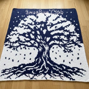 Könnte beinhalten: Eine marineblaue und weiße gehäkelte Decke mit einem Baumdesign. Der Baumstamm und die Äste sind marineblau, mit weißen Blättern und einem weißen Hintergrund. Der Text "SnugBlue Club" ist in Weiß.