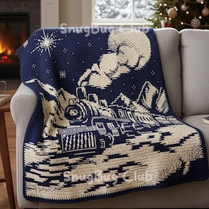 Könnte beinhalten: Eine marineblaue und cremefarbene Häkeldecke mit einer Zugszene unter einem Sternenhimmel. Die Decke zeigt einen Zug, Berge, einen Vollmond und einen Stern. Die Decke ist über ein graues Sofa drapiert.