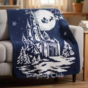 May include: A navy blue and white crocheted blanket with a castle design under a full moon and Santa's sleigh. The blanket is draped over a grey sofa. The text "SnugBug Club" is visible.