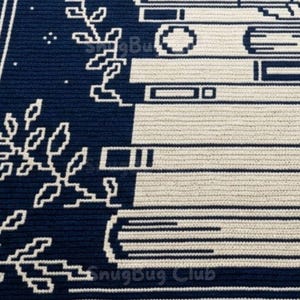 Pode incluir: Um t&ecirc;xtil azul marinho e creme apresenta um design de livros e motivos florais. O texto "SnugBug Club" &eacute; vis&iacute;vel na parte inferior. O padr&atilde;o &eacute; um design repetitivo, adequado para decora&ccedil;&atilde;o de casa ou aplica&ccedil;&otilde;es t&ecirc;xteis.