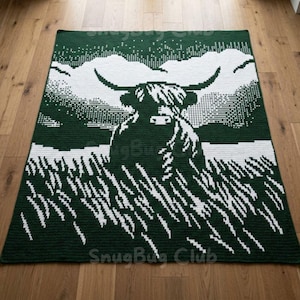 Puede incluir: Una manta de ganchillo verde oscuro y blanco con un diseño de vaca de las Tierras Altas. El diseño muestra la vaca en un campo con un cielo nublado. El texto "SnugBug Club" es visible en la esquina inferior derecha.