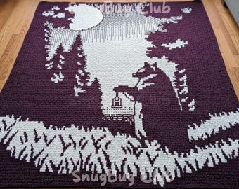 Pode incluir: Um cobertor de crochê com uma cena de floresta com lua cheia, árvores e uma casa com uma lanterna. O cobertor é principalmente roxo escuro com detalhes brancos. O texto "SnugBug Club" é visível.