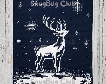 May include: A navy blue crocheted blanket featuring a white deer design with large antlers, snowflakes, and the text "SnugBug Club". The blanket has a winter theme and is likely handmade.