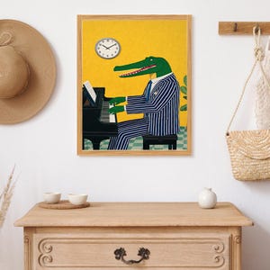 May include: A framed art print featuring an alligator in a blue and white striped suit playing a black piano. The background is yellow with a clock and a small plant. The artwork is in a wooden frame.