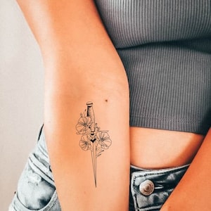 Puede incluir: Un tatuaje temporal en blanco y negro de una daga con flores.