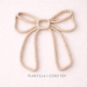 Könnte beinhalten: Eine beige gestrickte Schleife mit quadratischer Mitte und langen, herabhängenden Schlaufen. Die Schleife ist aus dickem, strukturiertem Garn gefertigt und wird auf hellem Hintergrund dargestellt. Der Text unten lautet "PLANTILLA I-CORD PDF".